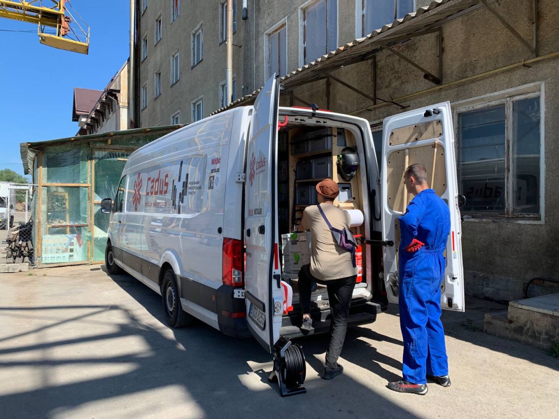 A transporter in front of a industry building with two people standing at the opened back door of the car.