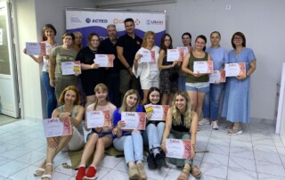 Ein Gruppenfoto in einem Gebäude. In zwei Reihen stehen und sitzen mehrere Absolventinnen eines Kurses, die fröhlich ihre Zertifikate halten. Inmitten der Frauen stehen zwei Kursleiter.