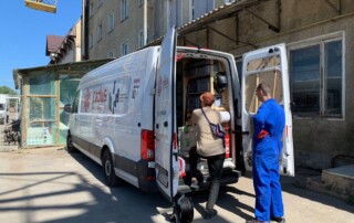 Ein Transporter mit zwei Personen an der geöffneten Hintertür vor einem Industriegebäude.