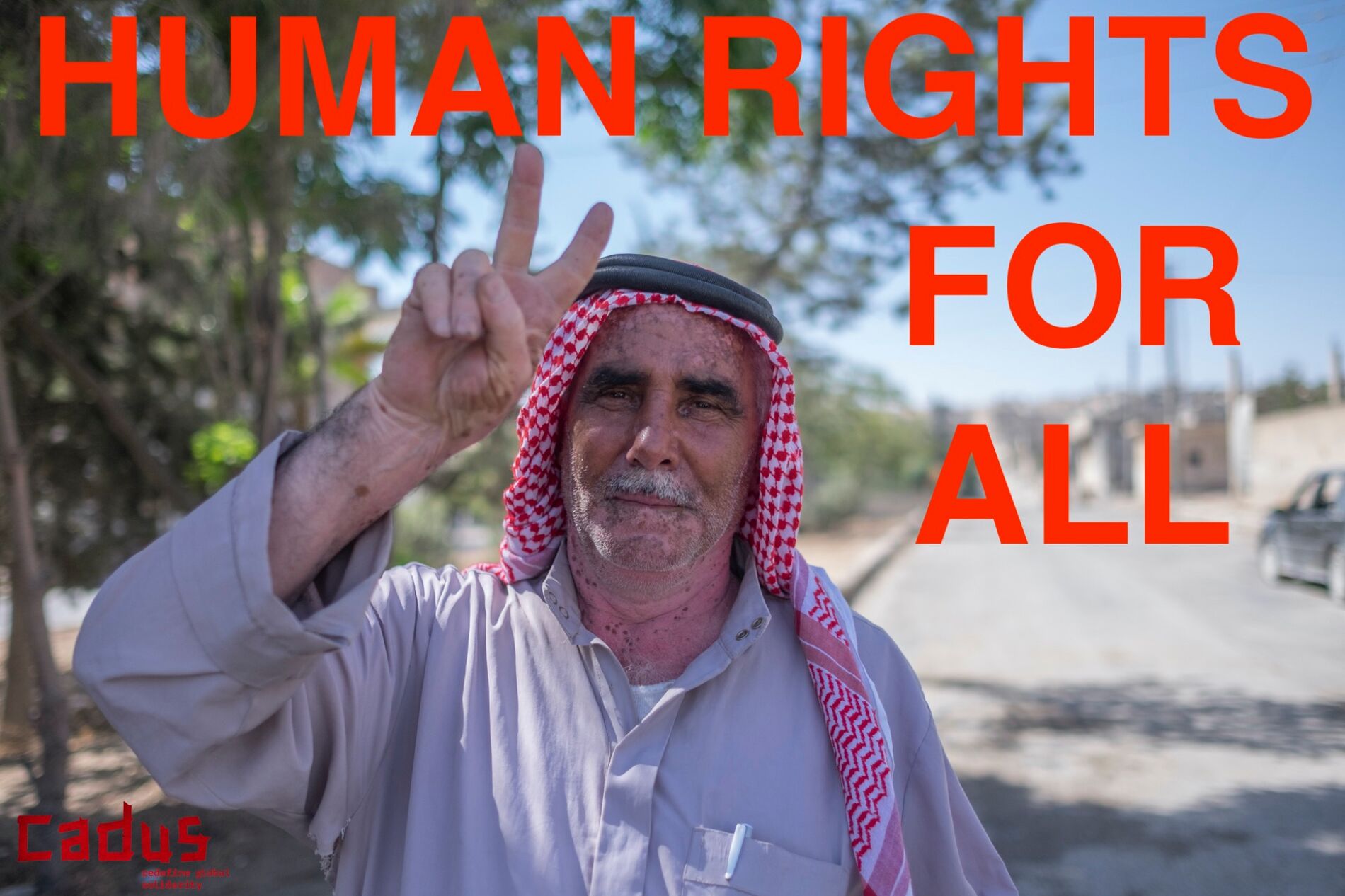 Ein Mann in Kobané mit traditioneller Kopfbedeckung lächelt und zeigt ein Peace-Zeichen. Dazu der Spruch: "Human Rights for all"