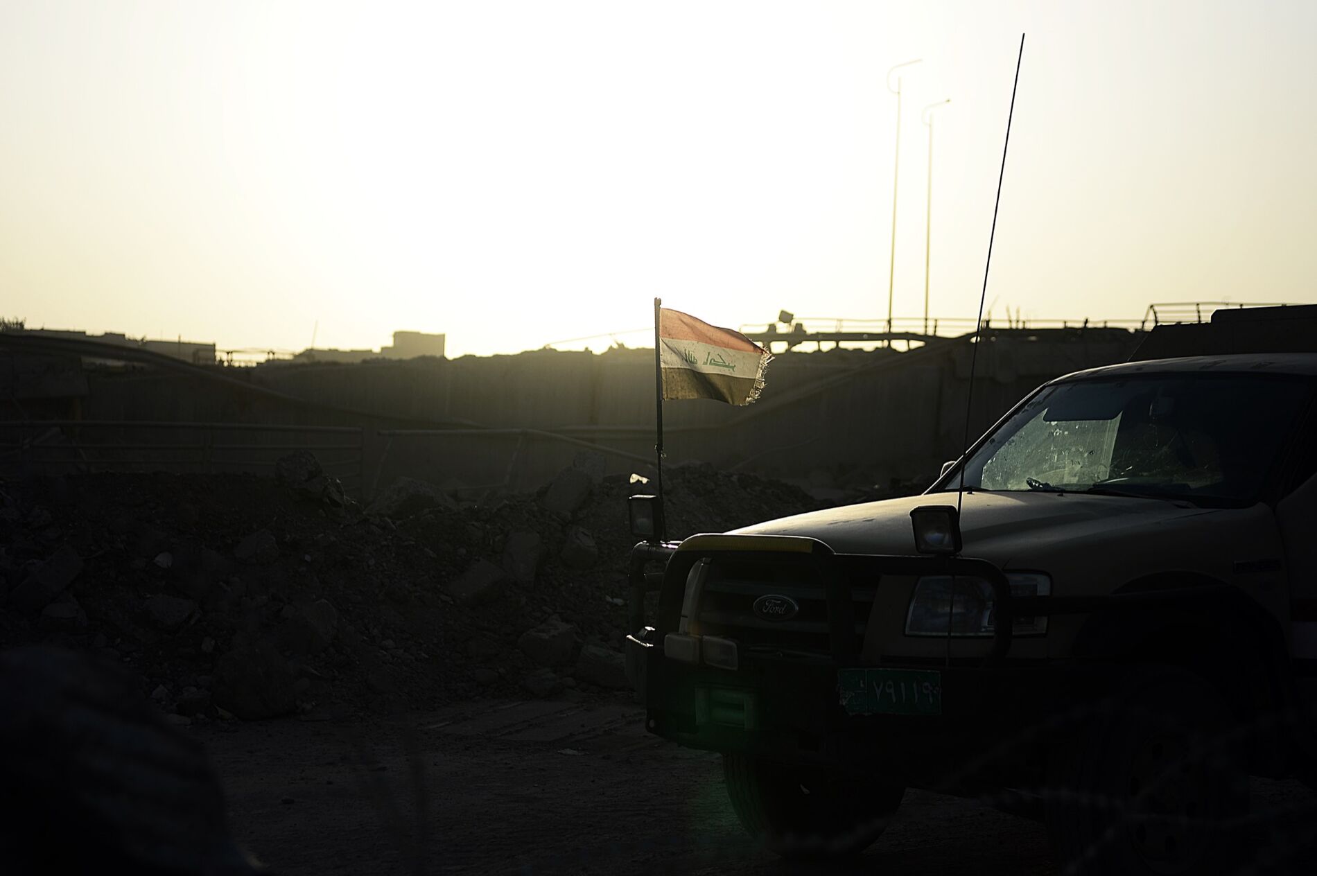 The sun rises behind a SUV with an Iraqi flag atached to it.