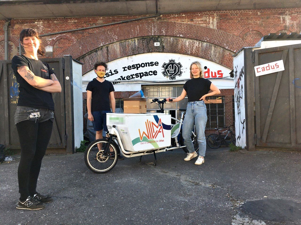 Drei Helfer*innen posieren mit einem Lastenrad vor dem CADUS Makerspace.