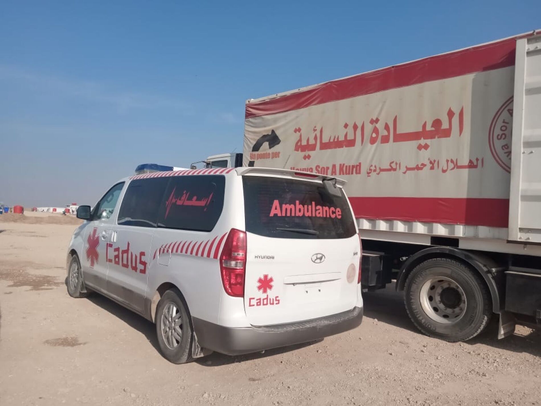 Ein Rettungswagen von CADUS steht vor einem LKW von Heyva Sor in Tal Tamr.