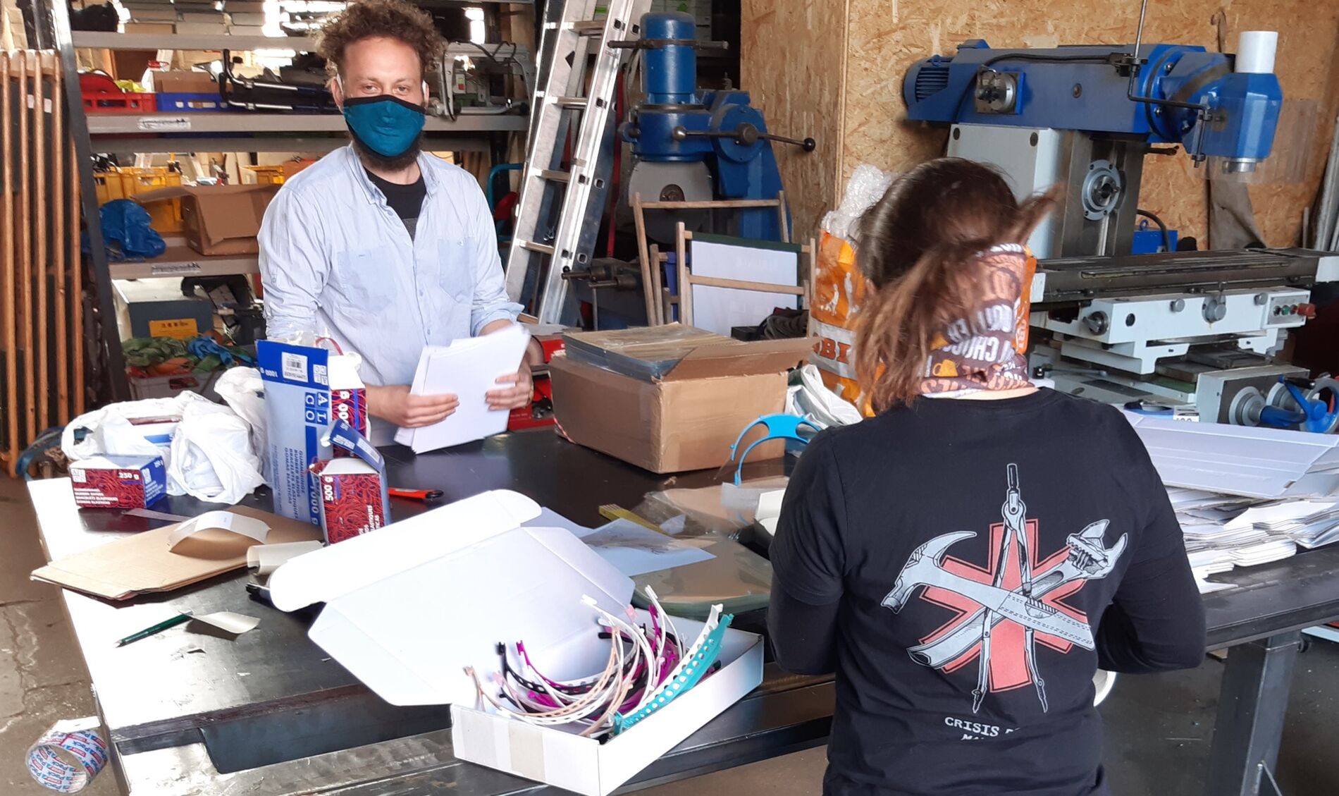 Two people packing face shields at a table, different tools and machines in the background.