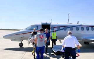 An airplane at the airport with four people in the front. Two of them carrying a patient stretcher.