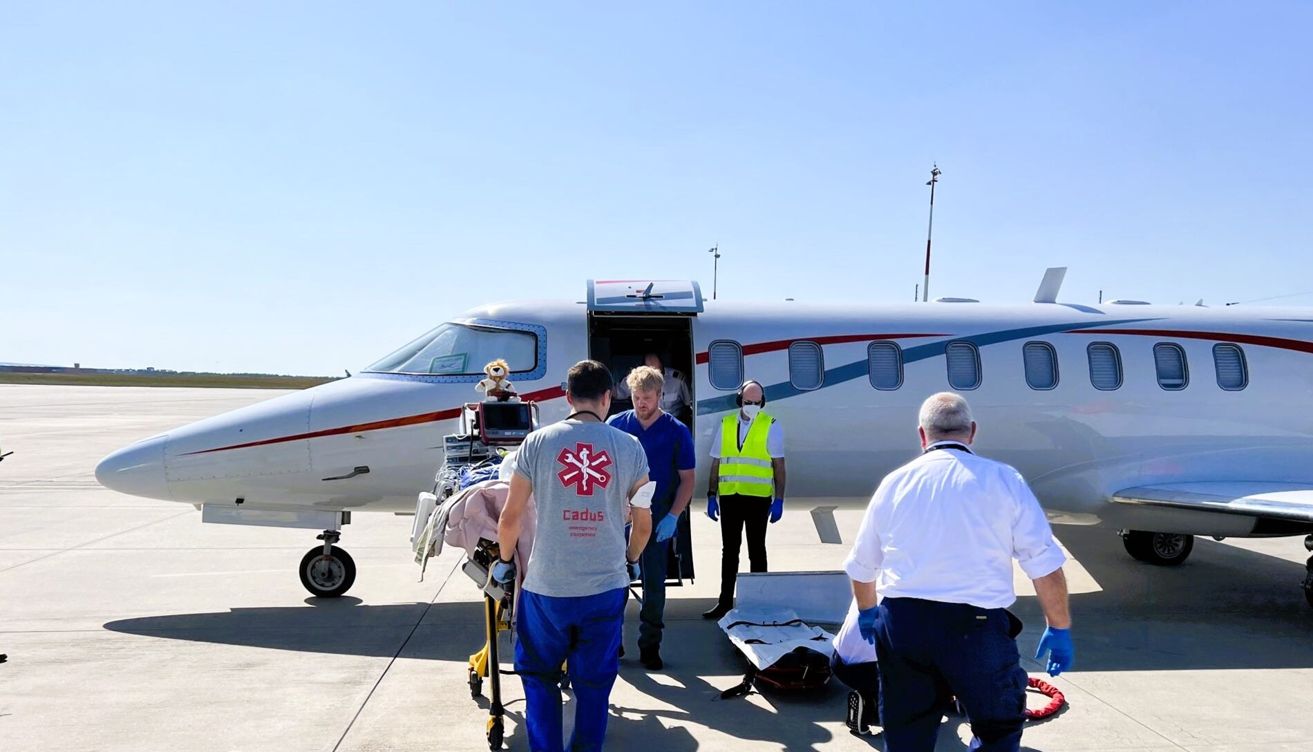 An airplane at the airport with four people in the front. Two of them carrying a patient stretcher.